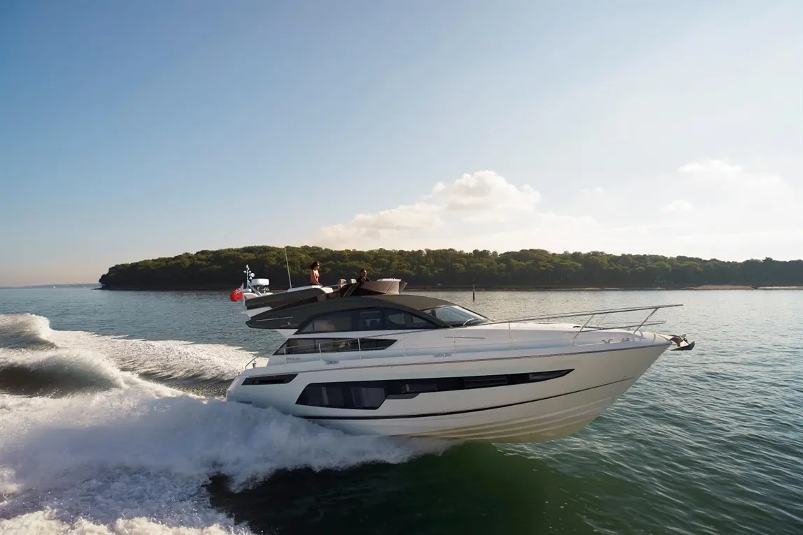 A sleek white motor yacht speeds across tranquil waters, with two people on the deck enjoying the ride.